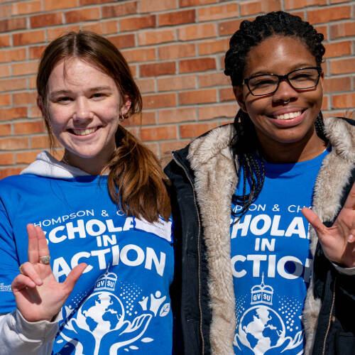 Two GVSU students smiling and holding fingers up in the shape of an anchor.